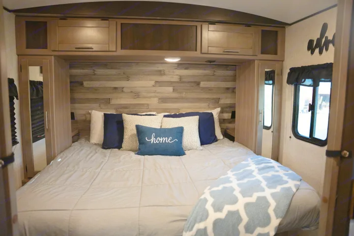 Cozy RV rental bedroom interior featuring a comfortable bed, wooden headboard, overhead cabinets, and a "home" pillow.. Crossroads RV Sunset Trail Super Lite 2022