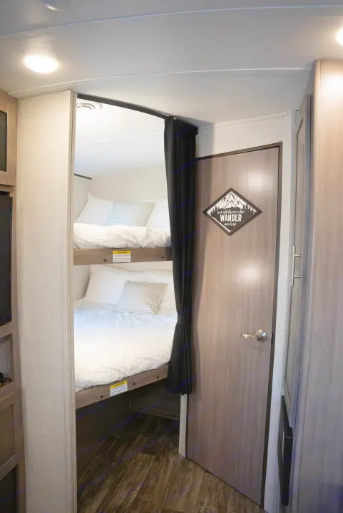 Inside this RV rental: a view of the sleeping area with two neatly made bunk beds, white bedding, and a privacy curtain.. Crossroads RV Sunset Trail Super Lite 2022