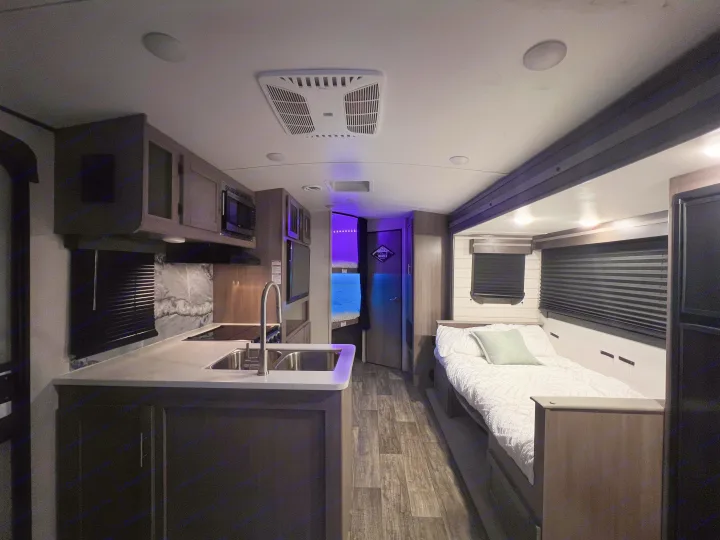 Tour this RV rental's sleek interior: kitchen, cozy bed, and playful bunk beds with vibrant purple and blue lighting.. Crossroads RV Sunset Trail Super Lite 2022