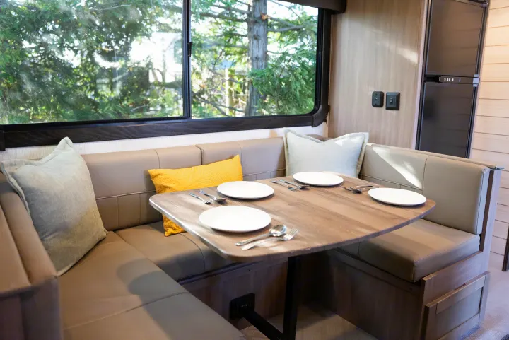 Inside an RV rental: a cozy dinette with wood-look table, set dishes, comfy bench seats, and a large window view.. Crossroads RV Sunset Trail Super Lite 2022