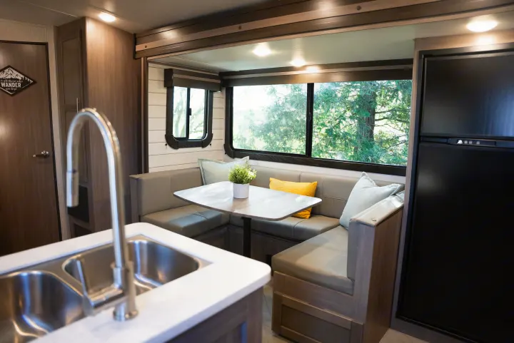 Cozy RV rental interior with a bright dinette, modern kitchen sink, and large windows revealing scenic trees.. Crossroads RV Sunset Trail Super Lite 2022