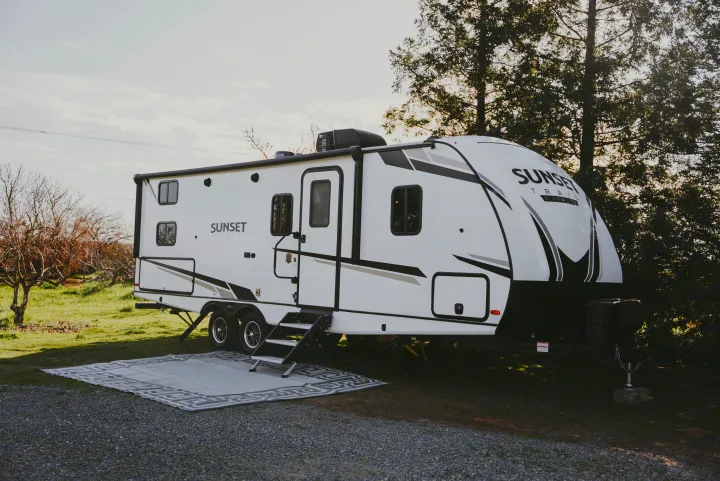 Enjoy the outdoors with an RV rental! A white Sunset Trail travel trailer is set up with an outdoor rug on gravel.. Crossroads RV Sunset Trail Super Lite 2022