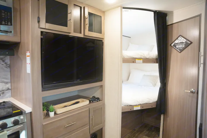 Cozy RV rental interior with twin bunk beds, a functional kitchen area, and a flat-screen TV.. Crossroads RV Sunset Trail Super Lite 2022