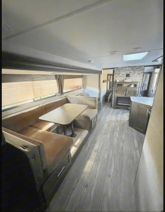 Spacious RV rental interior featuring a cozy U-shaped dinette, entertainment unit with faux brick accent, and wood-look flooring.. Forest River Cherokee Grey Wolf 2019