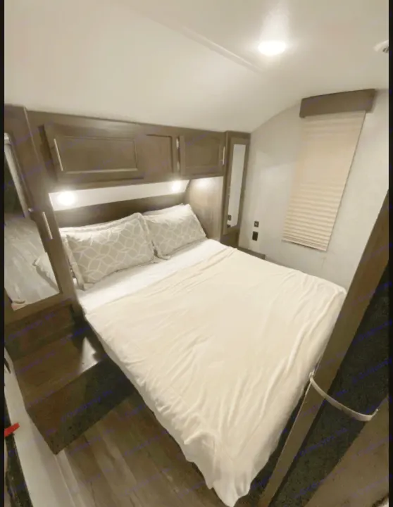 Cozy RV rental bedroom interior with dark wood cabinets, bed, and window blinds, offering comfortable sleeping.. Forest River Cherokee Grey Wolf 2019