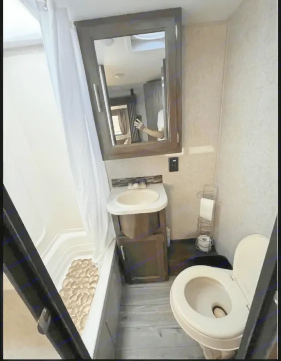 An RV rental's compact bathroom, showing a shower with curtain, sink, and toilet.. Forest River Cherokee Grey Wolf 2019