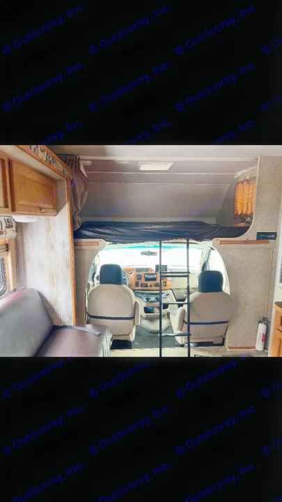 RV rental interior: View from living area towards front cabin, over-cab bunk bed, and driver/passenger seats.. Winnebago Chalet 2010
