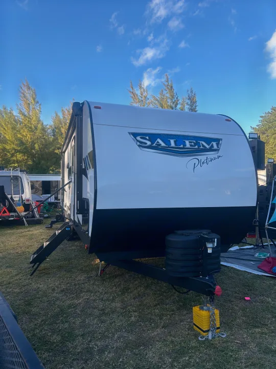 This white and black Salem Platinum rv rental travel trailer is ready for camping, parked on green grass under a blue sky.. Forest River 32BHDSX 2023