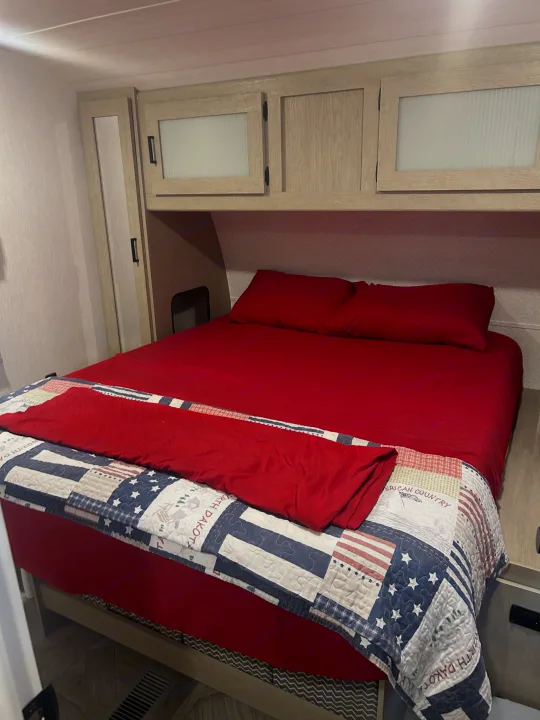 Cozy RV rental bedroom featuring red bedding, patriotic quilt, and light wood storage cabinets.. Forest River 32BHDSX 2023