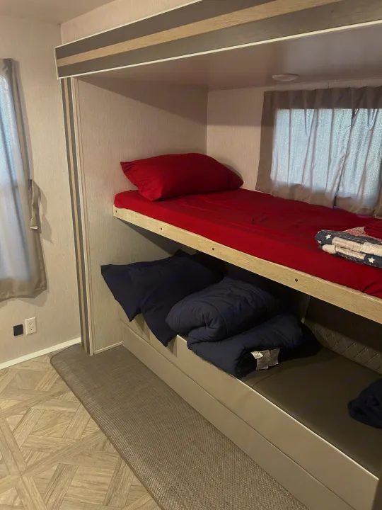 Cozy bunk beds inside an RV rental, featuring a red top bunk and a lower sleeping area with blue bedding. Ideal for travel.. Forest River 32BHDSX 2023