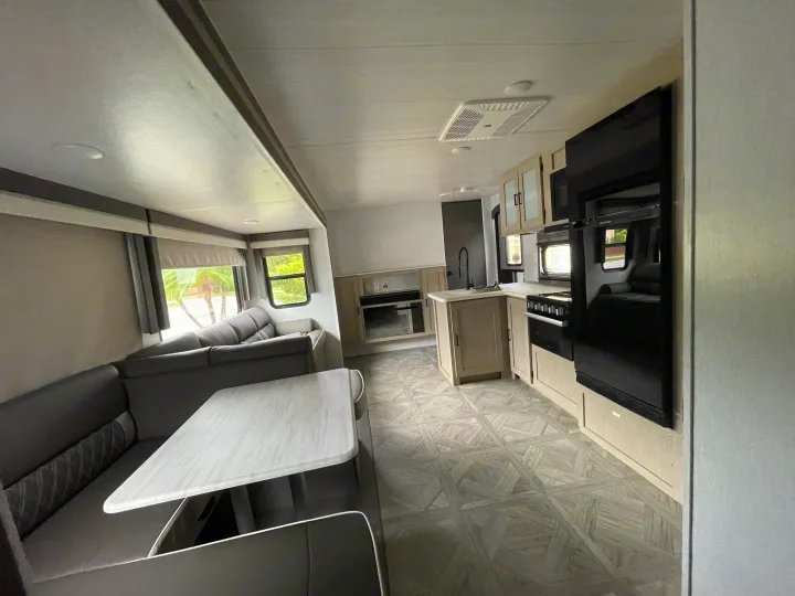 Spacious rv rental interior featuring a cozy living area with an L-shaped sofa and table, and a well-equipped kitchen.. Forest River 32BHDSX 2023