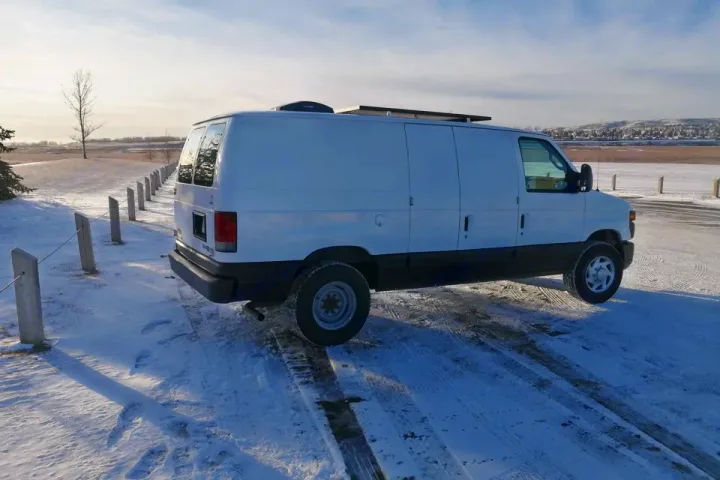 White converted camper van with solar panels, parked in snow. Your perfect RV rental for winter adventures.. Ford Ford E350 2011