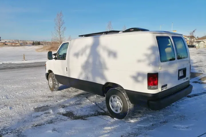 White RV rental camper van with rooftop solar panels & vent, parked on snow-covered ground in winter.. Ford Ford E350 2011