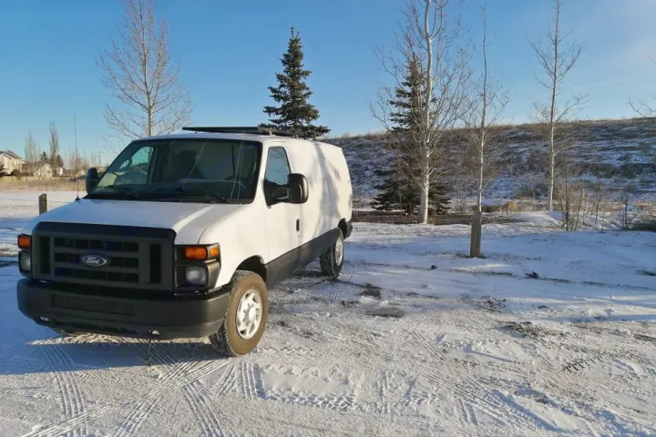 White Ford E-Series van, possibly an rv rental, parked on snowy ground. Winter landscape with trees and distant houses.. Ford Ford E350 2011