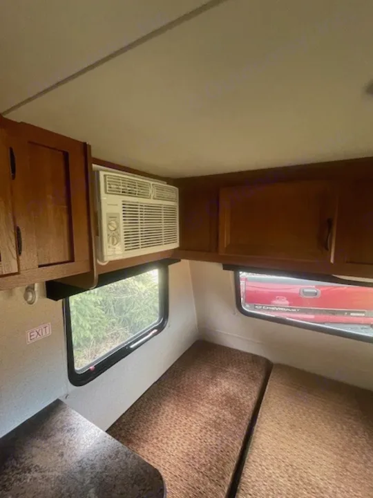 RV rental interior: window AC, wood cabinets, and cushioned benches. An 'EXIT' sign is near a window, with trees visible outside.. Jayco Jay Flight SLX 2015