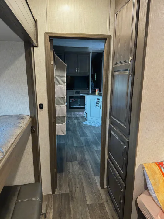 RV rental interior: Bunk beds and storage on either side of a doorway leading to the living area with a fireplace.. Keystone RV Cougar 2023