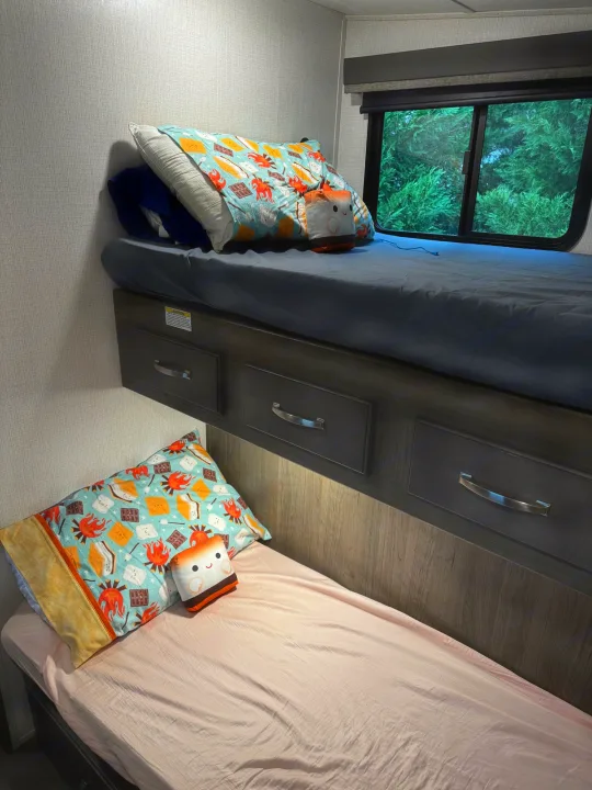 Inside an rv rental, cozy bunk beds with s'mores pillows, storage drawers, and a window view. Ideal family sleep space.. Keystone RV Cougar 2023