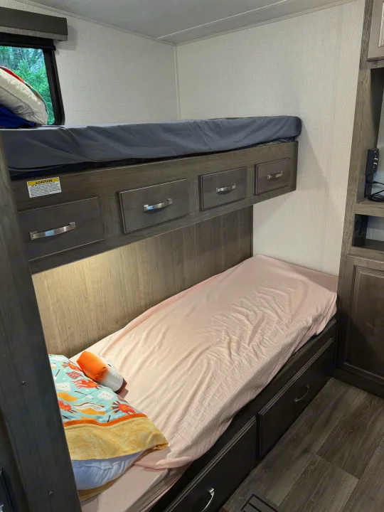 This cozy RV rental features bunk beds with dark wood drawers beneath each, providing ample storage for your journey.. Keystone RV Cougar 2023