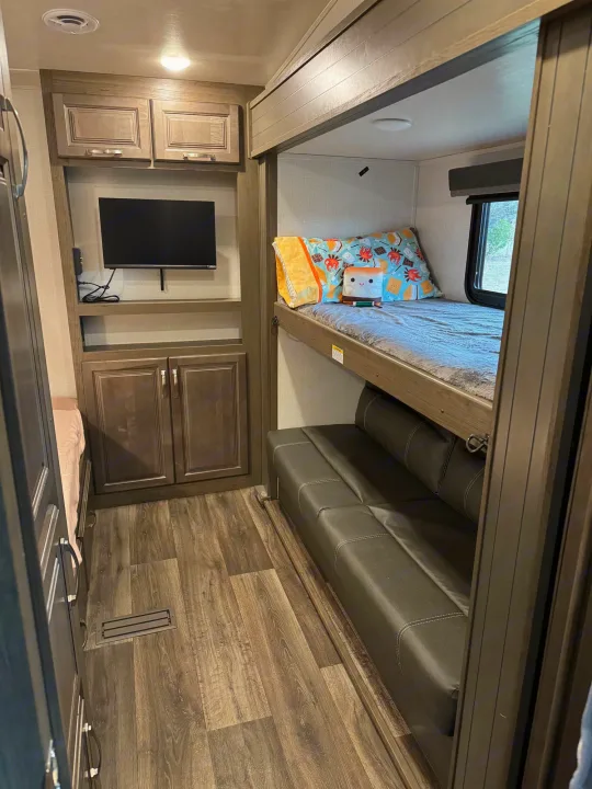 This RV rental interior features bunk beds, a lower sofa/bed, TV, and ample storage, ideal for travel comfort.. Keystone RV Cougar 2023
