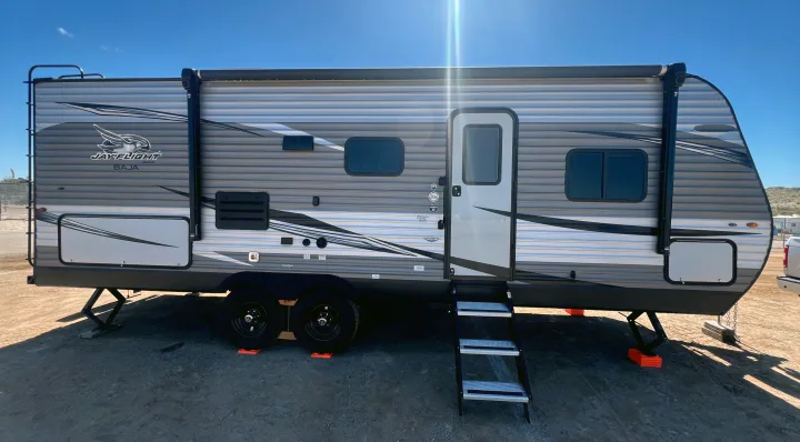 A modern Jay Flight Baja travel trailer, ideal for an RV rental, parked outdoors with its steps down and stabilizing jacks.. Jayco Jay Flight SLX 2021