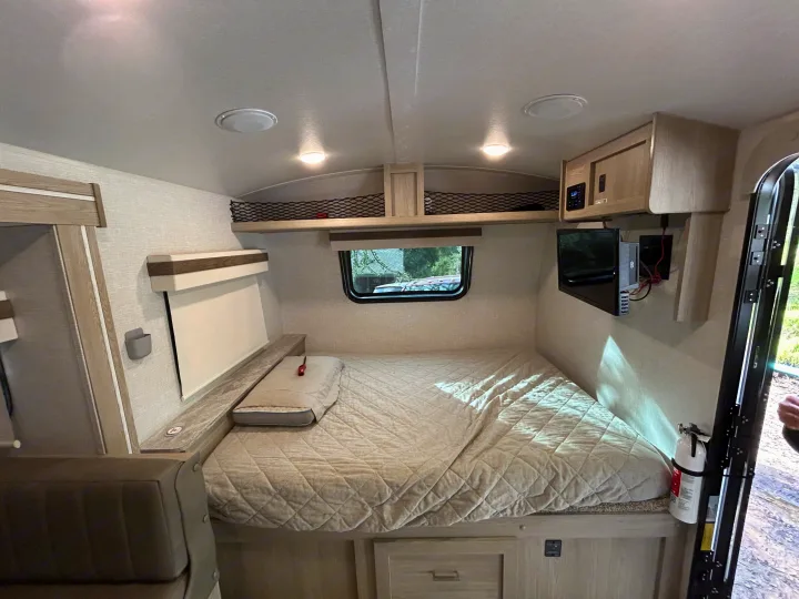 Cozy RV rental sleeping area featuring a quilted bed, overhead storage, small TV, and a fire extinguisher for safety.. Geo pro Geo pro by rockwood 2022