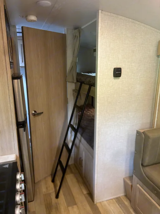RV rental interior with bunk beds, ladder, fridge, thermostat, and an open door to another area.. Geo pro Geo pro by rockwood 2022