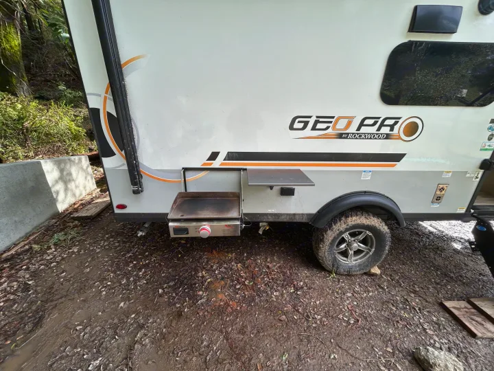 This Geo Pro RV rental offers an outdoor griddle and table, set in a muddy campsite. Ready for adventure!. Geo pro Geo pro by rockwood 2022
