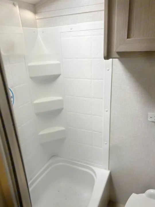 RV rental bathroom: Compact white shower/tub with built-in shelves. Textured walls and a toilet visible. Ready for your trip!. Geo pro Geo pro by rockwood 2022