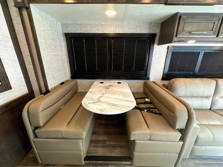 RV rental dinette area: tan booth seating with seatbelts, marble table, and large windows in a spacious camper interior.. Entegra Coach Vision XL 2025