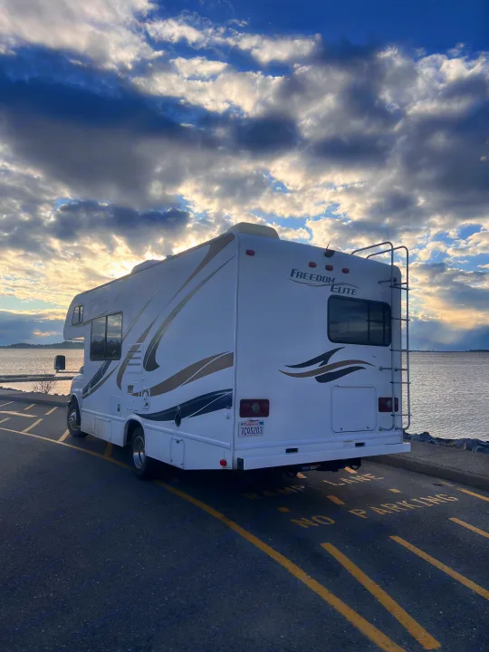 Freedom Elite rv rental by the water, parked on asphalt with dramatic sunset clouds. Ideal for California road trips.. Thor Freedom Elite 2014