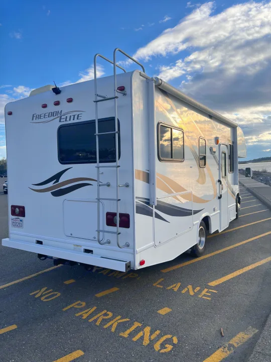 Class C rv rental by the water at a 'no parking' ramp, reflecting golden hour clouds. Ideal for outdoor adventures.. Thor Freedom Elite 2014