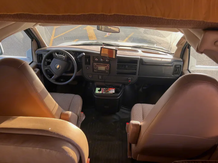 Inside a modern RV rental: A detailed view of the Chevrolet van's dashboard, steering wheel, and comfortable front seats.. Thor Freedom Elite 2014