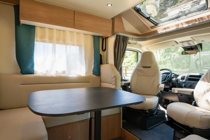 Bright RV rental interior showing dining table, bench seats, and driver's cabin. Perfect for travel adventures.. JOA 75Q 2024