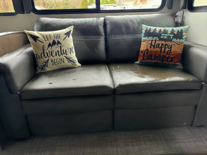 Sofa inside an RV rental with two "adventure" themed pillows, showing extensive water stains on cushions.. Keystone RV Cougar 2023