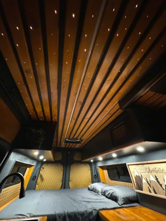 Step into this cozy RV rental's custom interior! Features a unique starry wood ceiling, comfy bed, and warm ambiance for adventures.. Mercedes-Benz Sprinter 2020