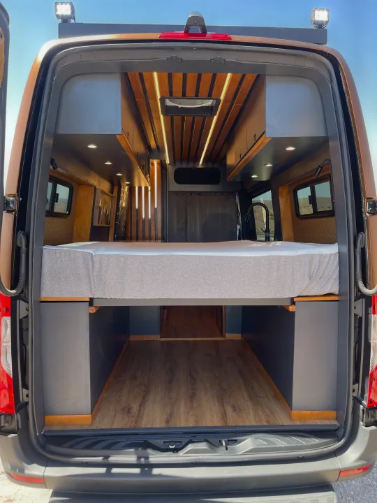 Inside a premium RV rental: a custom van conversion with raised bed, under-bed storage, wood-slat ceiling, and LED lighting.. Mercedes-Benz Sprinter 2020