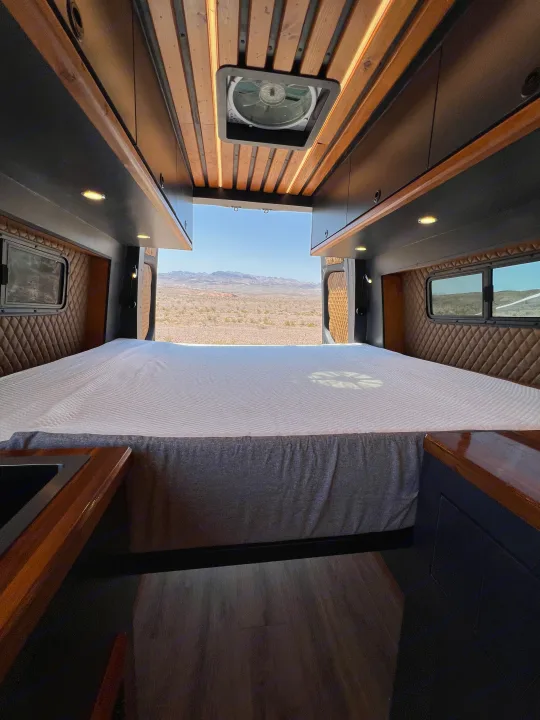 Serene RV rental interior: cozy bed, warm lighting, and expansive desert views from the open rear doors.. Mercedes-Benz Sprinter 2020