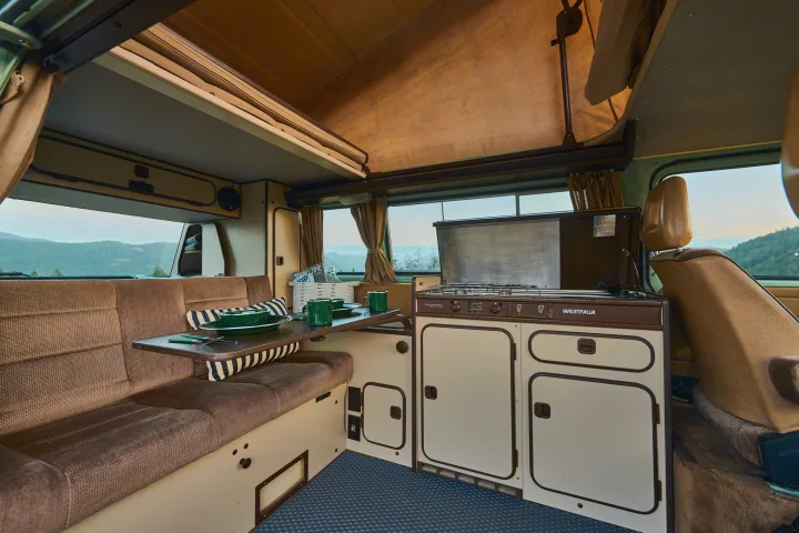 Experience vintage adventures with our RV rental! Inside a classic Westfalia camper, featuring a pop-top roof, kitchen, and cozy living area.. Volkswagen T3 Westfalia 1986