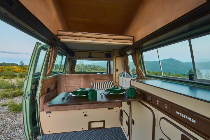 Vintage Westfalia camper van interior, dining setup amidst scenic views. An ideal RV rental for your next outdoor adventure.. Volkswagen T3 Westfalia 1986