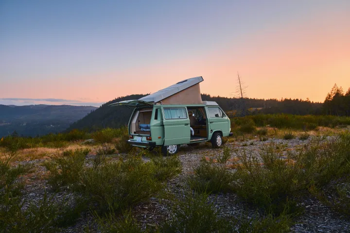 A light green pop-top VW camper van, doors open, parked in nature at sunset. Ideal for your next rv rental adventure.. Volkswagen T3 Westfalia 1986