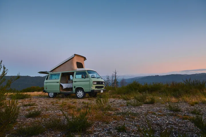 A light green pop-top camper van parked at dusk, side door open, ready for adventure. Explore nature with an RV rental.. Volkswagen T3 Westfalia 1986