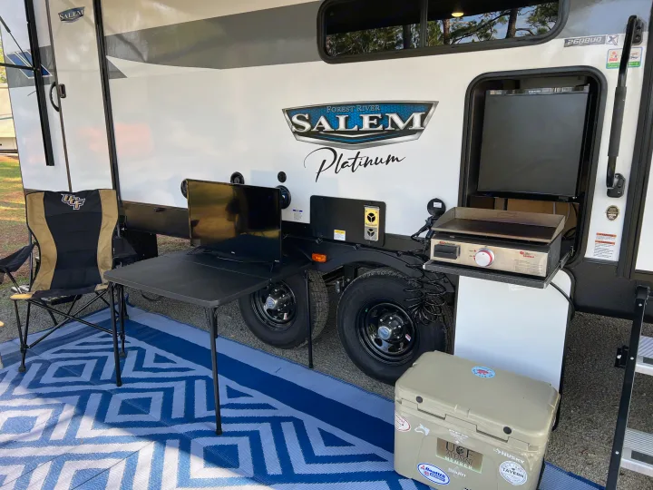 RV rental with a comfortable outdoor living area, featuring a TV, griddle, and cooler on a blue patio mat.. Forest River Salem FSX Platinum 2023