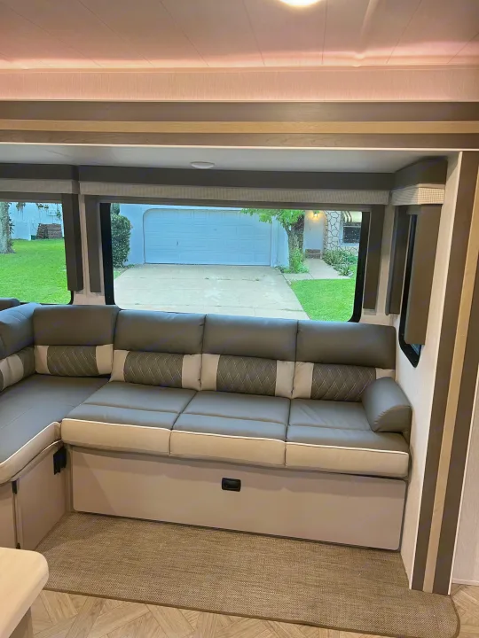 An inviting RV rental interior showing a comfortable sectional sofa and large windows with a view of a home's driveway.. Forest River Salem FSX Platinum 2023