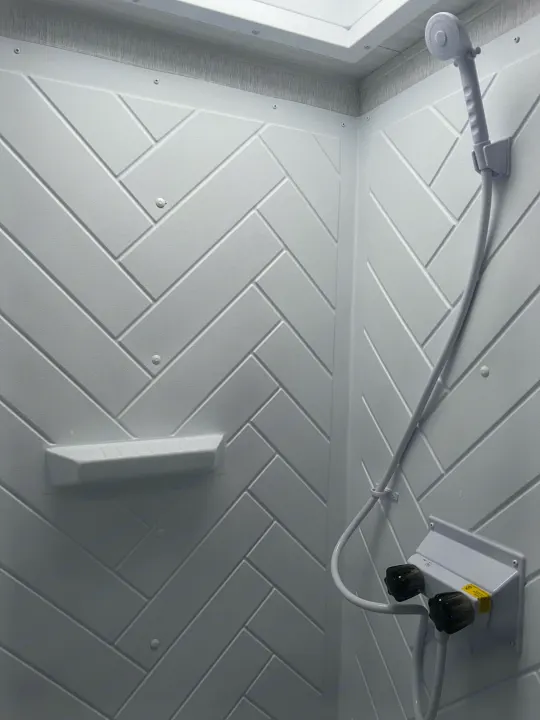 Bright RV rental shower stall with white herringbone walls, handheld showerhead, shelf, and water controls.. Forest River Salem FSX Platinum 2023