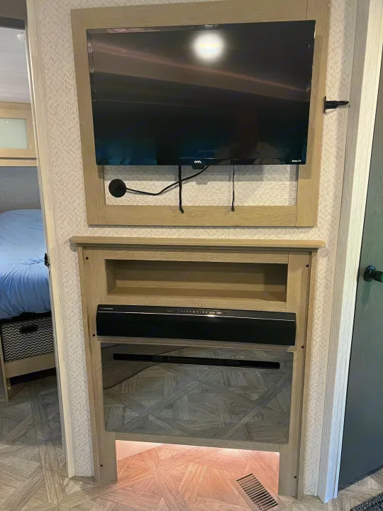 Modern RV rental interior with a wall-mounted TV, soundbar, and electric fireplace, next to a bed.. Forest River Salem FSX Platinum 2023
