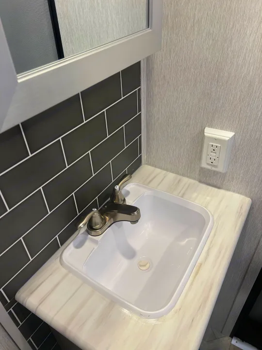 Modern RV rental bathroom sink with white countertop, dark grey subway tile backsplash, chrome faucet, and GFCI outlet.. Forest River Salem FSX Platinum 2023