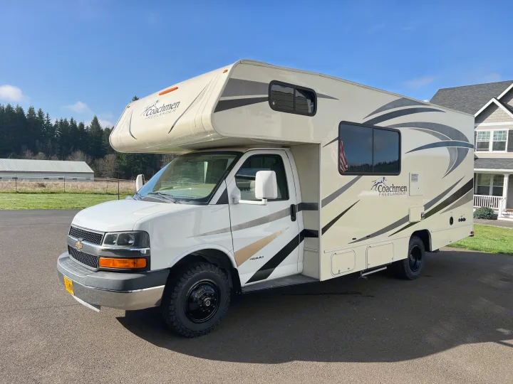 White Coachmen Freelander Class C RV rental, parked on asphalt. Scenic outdoor setting with trees and a house visible.. Forest River Coachmen Freelander 2017