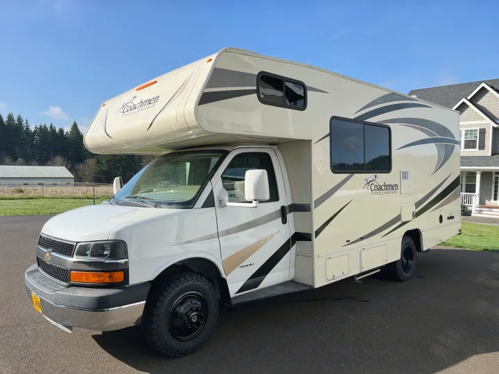 This Class C Coachmen Freelander RV rental, painted white and beige with dark stripes, is parked on asphalt, ready for adventure.. Forest River Coachmen Freelander 2017