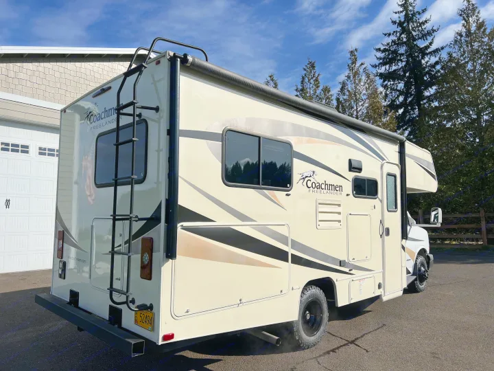 This Coachmen Freelander RV rental, a cream motorhome with black/tan graphics and a back ladder, is parked on asphalt.. Forest River Coachmen Freelander 2017