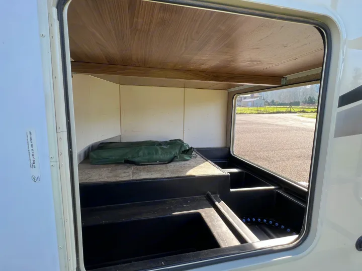 Inside an **rv rental**'s spacious pass-through storage bay, revealing utility bins & space for gear like a green camp chair bag.. Forest River Coachmen Freelander 2017